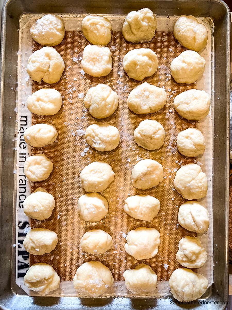 A baking sheet covered with a silicone baking sheet and dipped dough for pretzel balls.