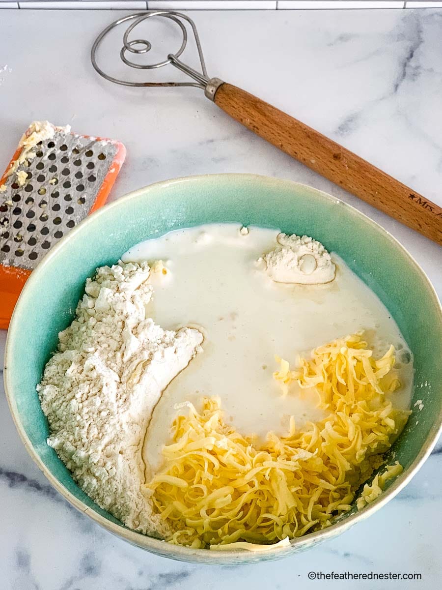 A bowl of biscuit ingredients with grater and dough whisk.