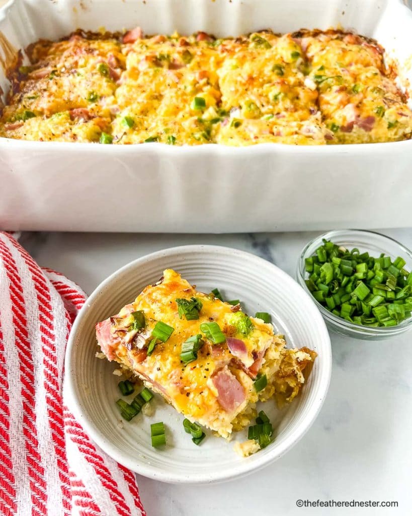 Serving of ham and tater tot casserole with the casserole dish in the background.