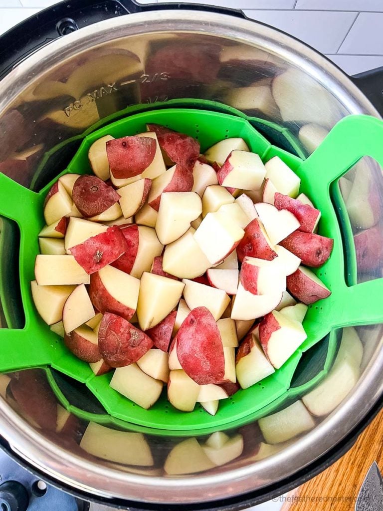 cubed potatoes in Instant Pot with a green steamer basket containing the potatoes
