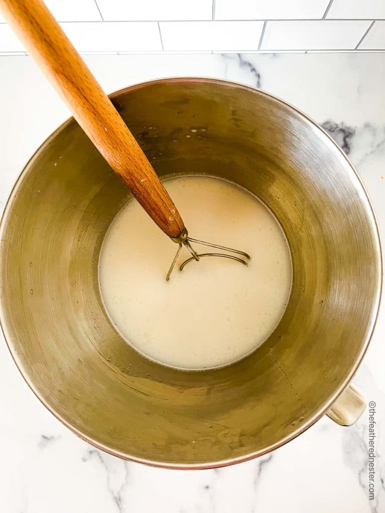 a stainless steel mixing bowl with milk, water, and sugar for making whole wheat bread dough.