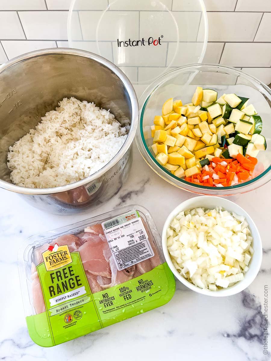 a package of chicken tenders, a bowl of diced veggies, a bowl of chopped onions, and a pot of cooked rice to make Blackstone Chicken Fried Rice.