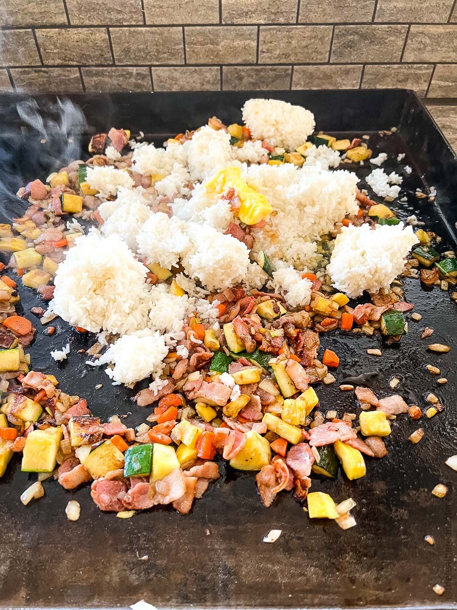 vegetables cooking on a griddle with rice added in.
