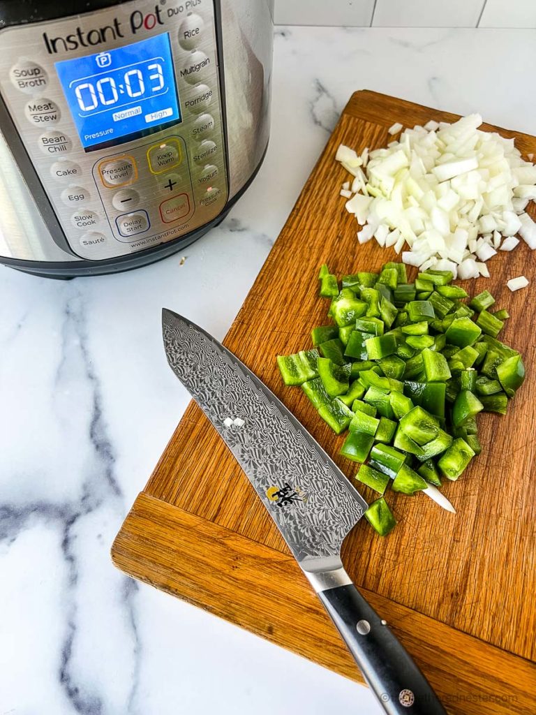 a cutting board with bell pepper, onions, and a knife with the Instant Pot in the background