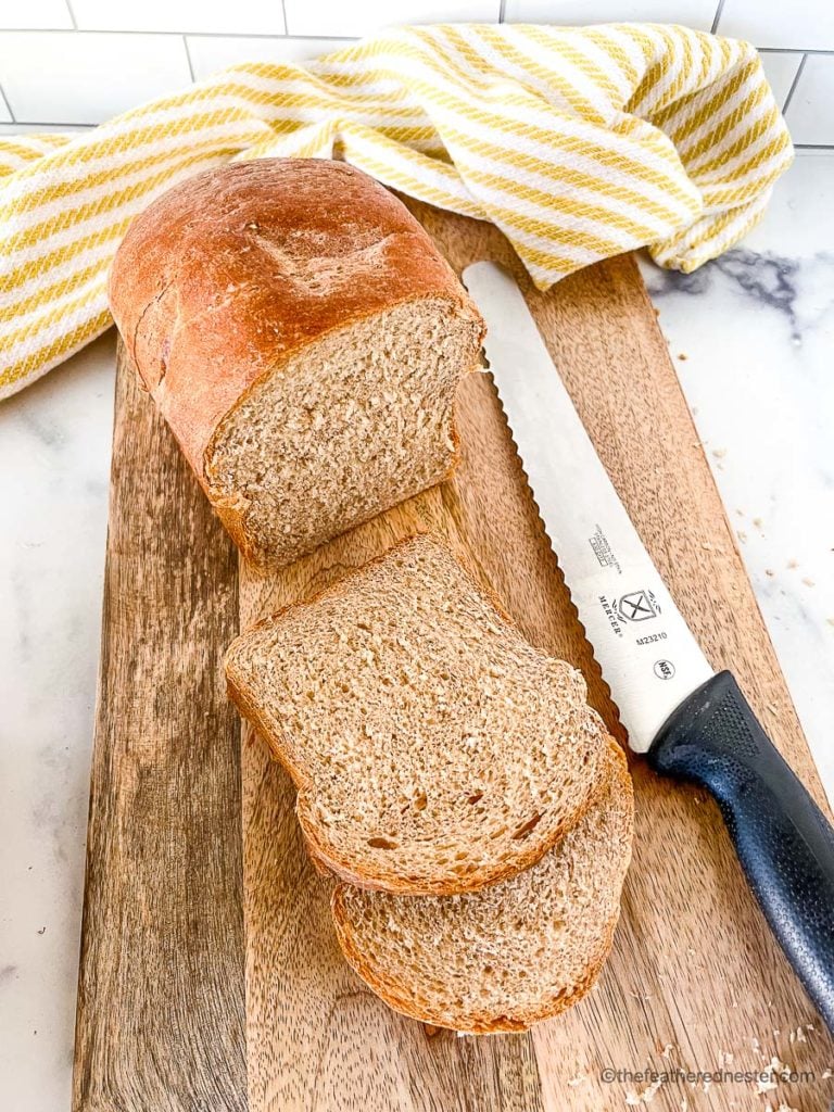 sliced whole wheat sandwich bread on a bread board with a knife and yellow and white kitchen towel and bread knife