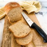 sliced whole wheat sandwich bread on a bread board with a knife and yellow and white kitchen towel and bread knife