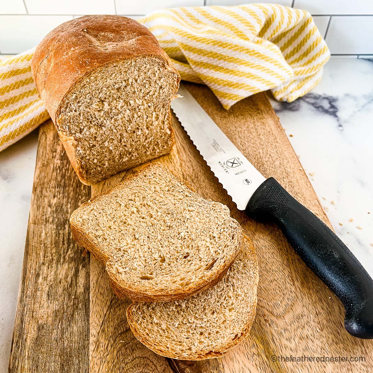 sliced whole wheat sandwich bread on a bread board with a knife and yellow and white kitchen towel and bread knife.