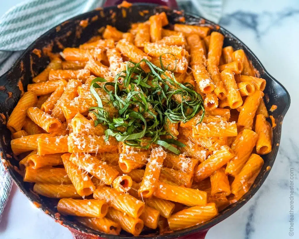 skillet with rigatoni with creamy vodka sauce with basil on top and shredded parmesan cheese