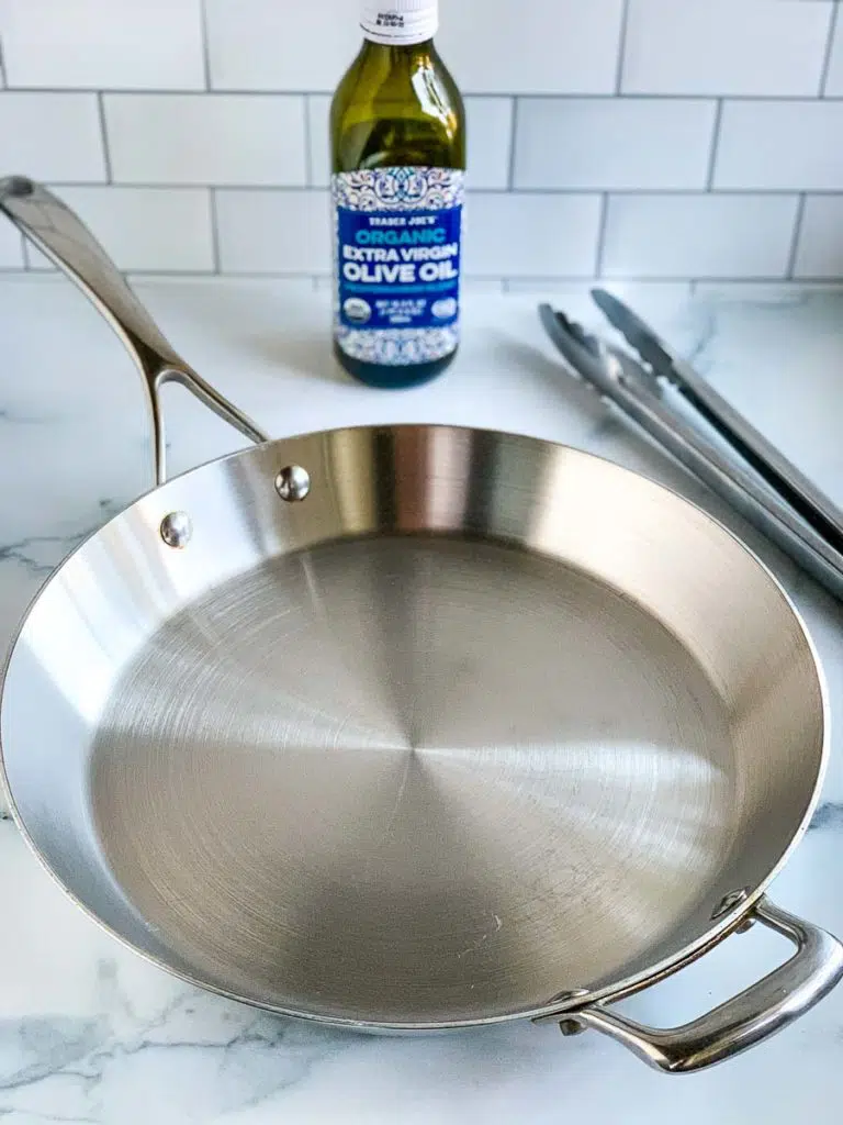 a stainless steel skillet with a tong and olive oil bottle in the background.