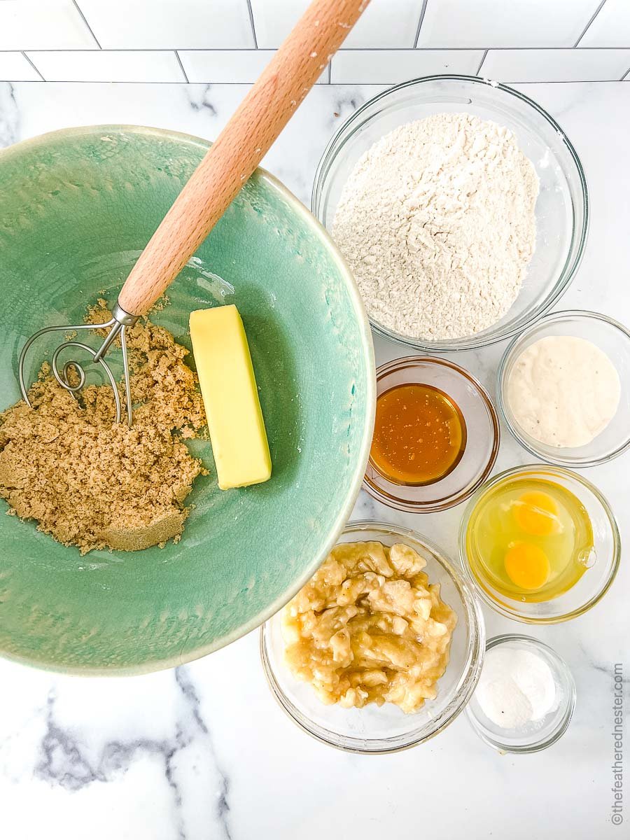 A green bowl with brown sugar and butter, (starting clockwise) clear bowls of flour, sourdough starter discard, eggs, salt, baking soda, baking flour, mashed bananas, vanilla.