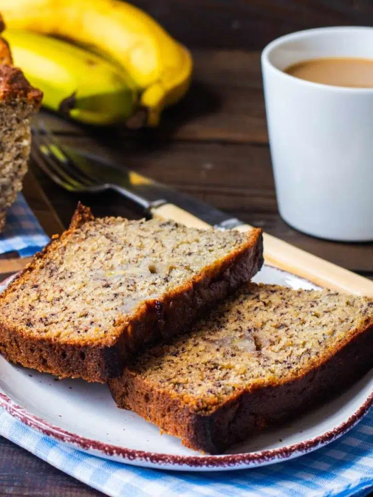 slices of banana bread with a cup of coffee on the right and bananas in the background