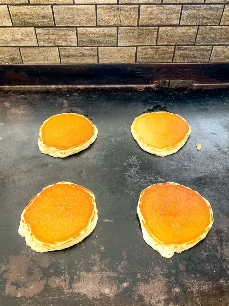 four pancakes cooking on a flat top grill