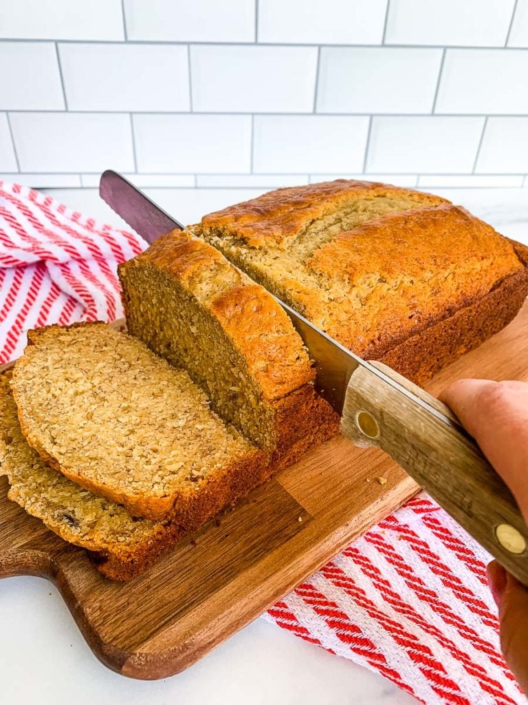 slicing banana bread self rising flour on a wooden board with a red and white kitchen towel