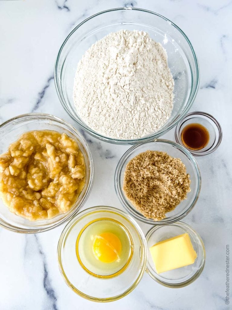 clear bowls of ingredients to make quick bread: mashed bananas, flour, brown sugar, eggs, butter, and vanilla.