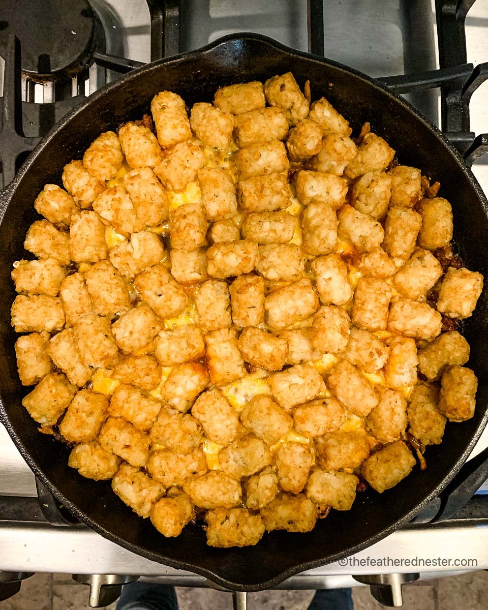 a skillet of green bean casserole with tater tots, ready to go into the oven.