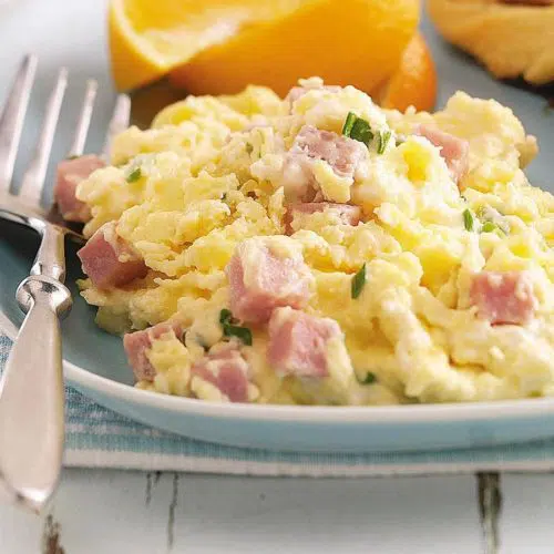 a plate of scrambled eggs with ham and a fork to the left of the eggs