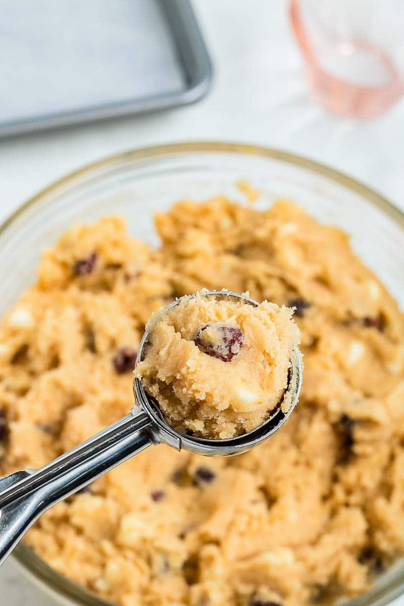 A scoop of cookie dough with the bowl of it in the background.