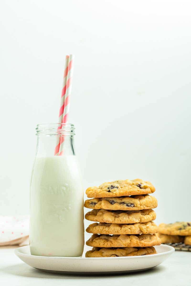 A bottle of milk with a straw next to a stack of cookies on a white plate.