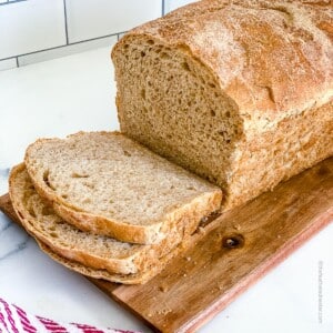 a square photo of a slice whole wheat sourdough sandwich bread on top of a wooden board.