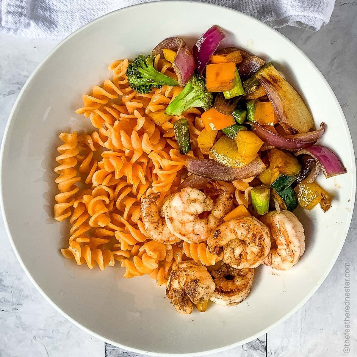 a white plate of Blackstone Vegetables with pasta and shrimp.