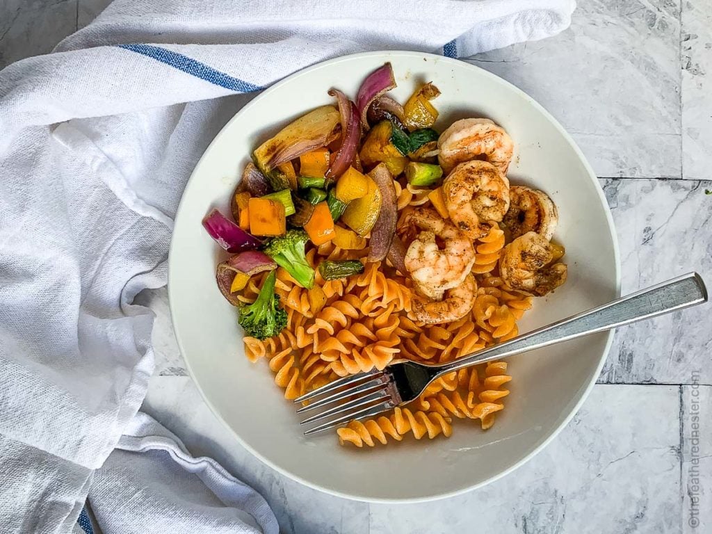 a white plate of grilled veggies, rotini pasta and shrimp cooked on a flat top grill
