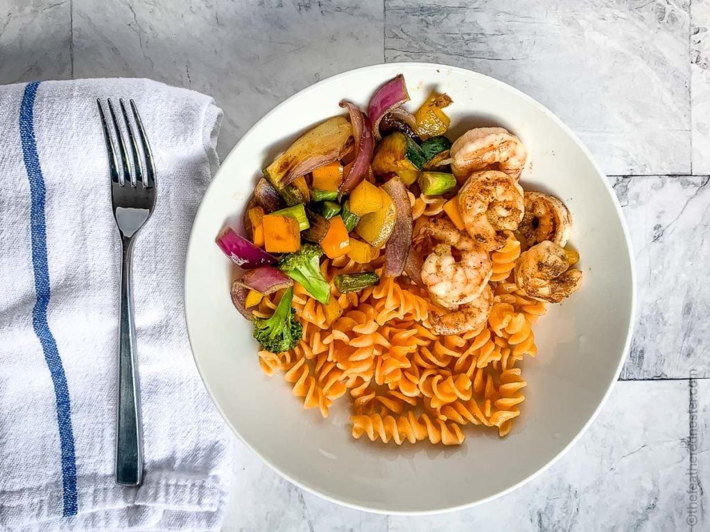 a white plate of pasta and grilled shrimp, and a white plate of grilled veggies, rotini pasta and shrimp with vegetables cooked on a flat grill