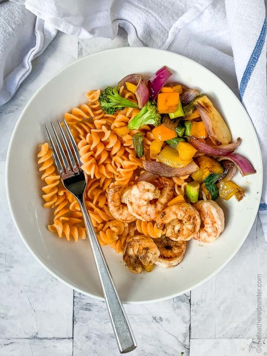 a white plate of pasta and grilled shrimp, and a white plate of grilled veggies, rotini pasta and shrimp with vegetables cooked on a Blackstone Griddle.