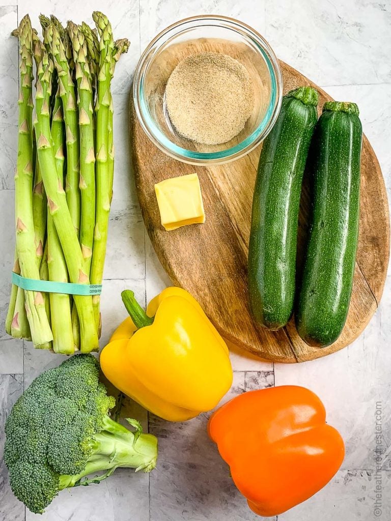zucchini, butter and spices on a wooden cutting board with bell peppers, broccoli, and asparagus for making Blackstone vegetables