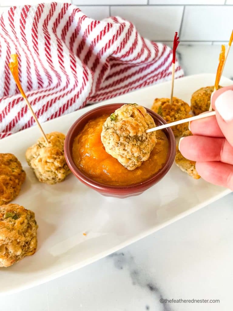 a bowl of mango sweet chili sauce with a sausage ball being dipped in the sauce on a white tray with a red and white napkin in the background