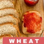 a sliced loaf of whole wheat sandwich bread with a slice spread with strawberry jam on a wooden bread board