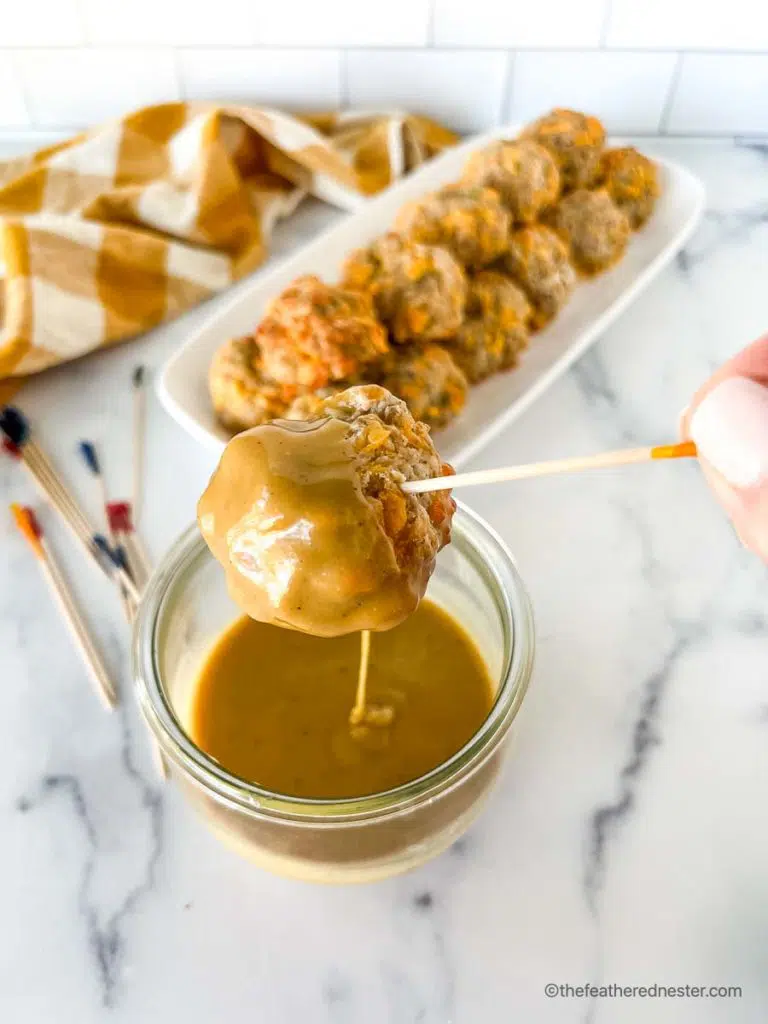 dipping easy sausage balls into a spicy hot mustard sauce in a clear weck jar