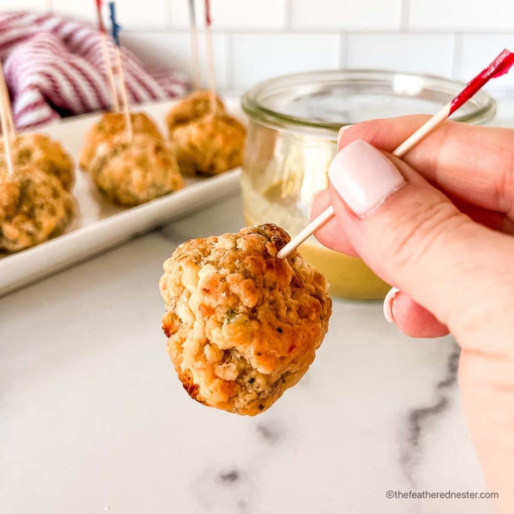 a skewered meatball made with this sausage ball recipe with a tray of pimento cheese balls in the background