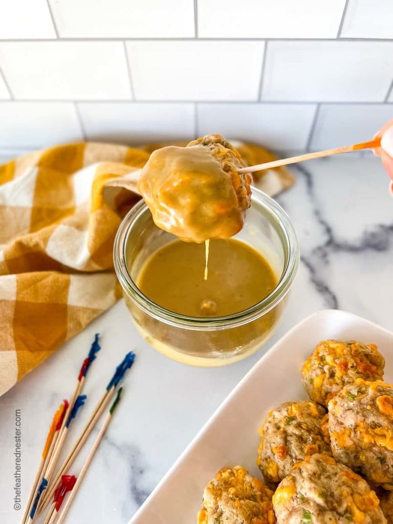 Turkey sausage balls on a platter, and one on a toothpick, being dipped into mustard sauce.