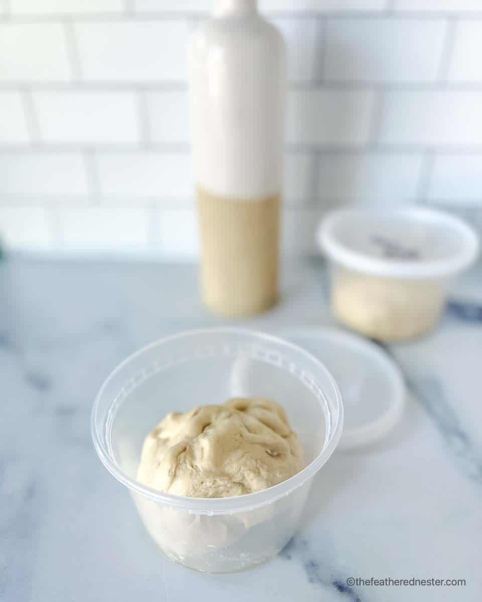 a storage container with a pizza dough ball for storing pizza dough in the fridge, along with a bottle of oil.