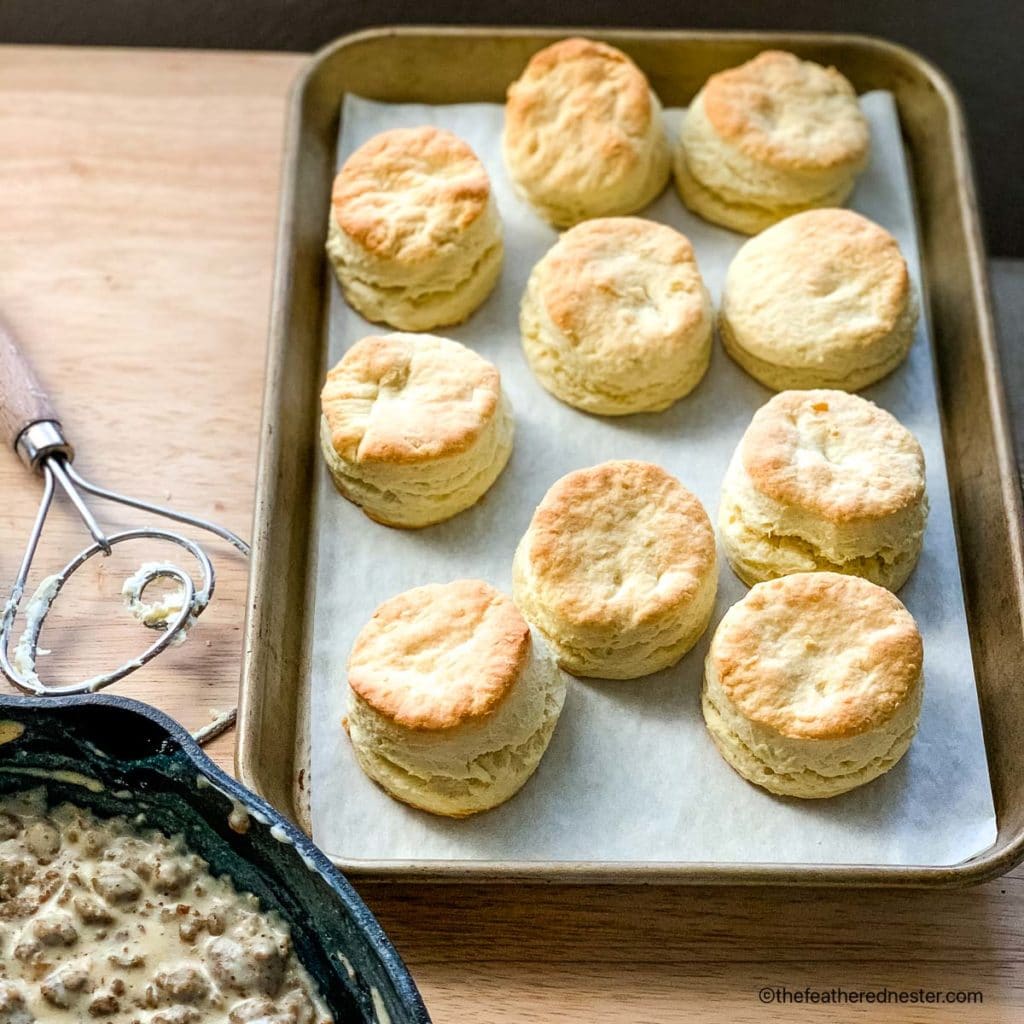a baking sheet of baked biscuits with a skillet of turkey sausage gravy