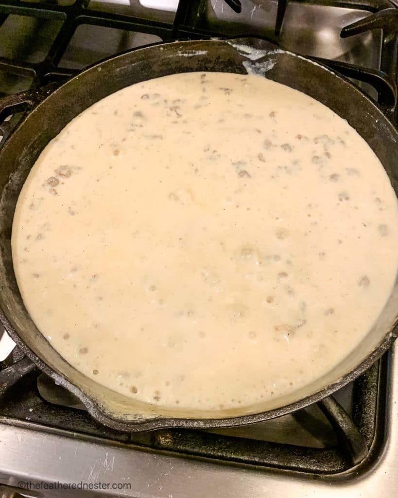 a cast iron skillet of sausage and milk simmering on the stove