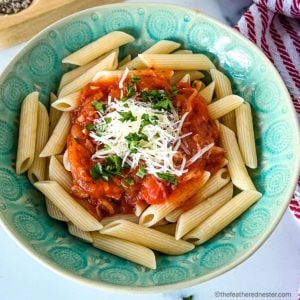a green serving bowl with rigatoni pasta with a rich Italian tomato sauce.
