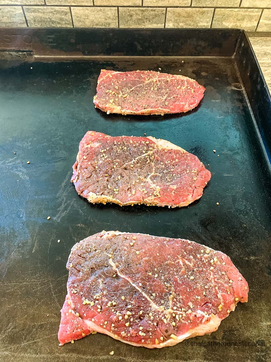 Cooking the raw steaks on the griddle.