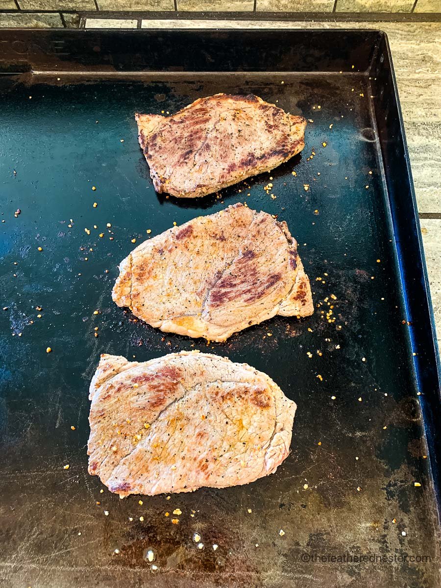 Seared steaks on top of a griddle.