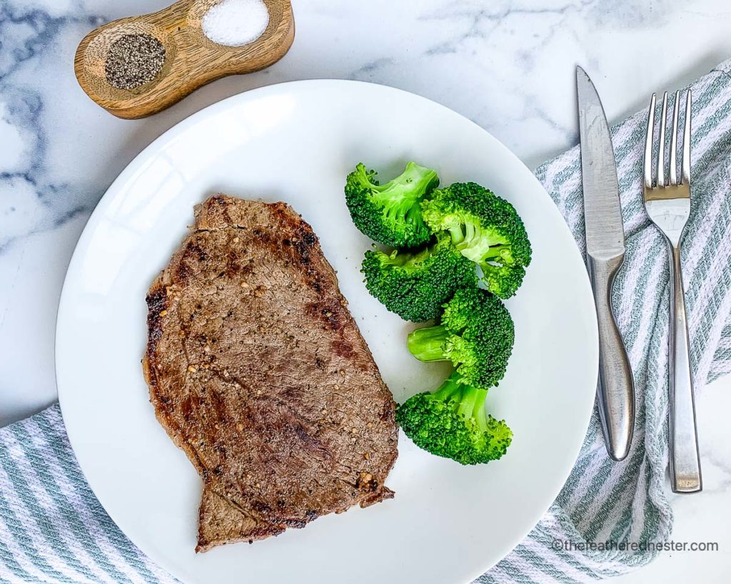 hibachi steak with broccoli on a white plate with silverware and a blue and white napkin