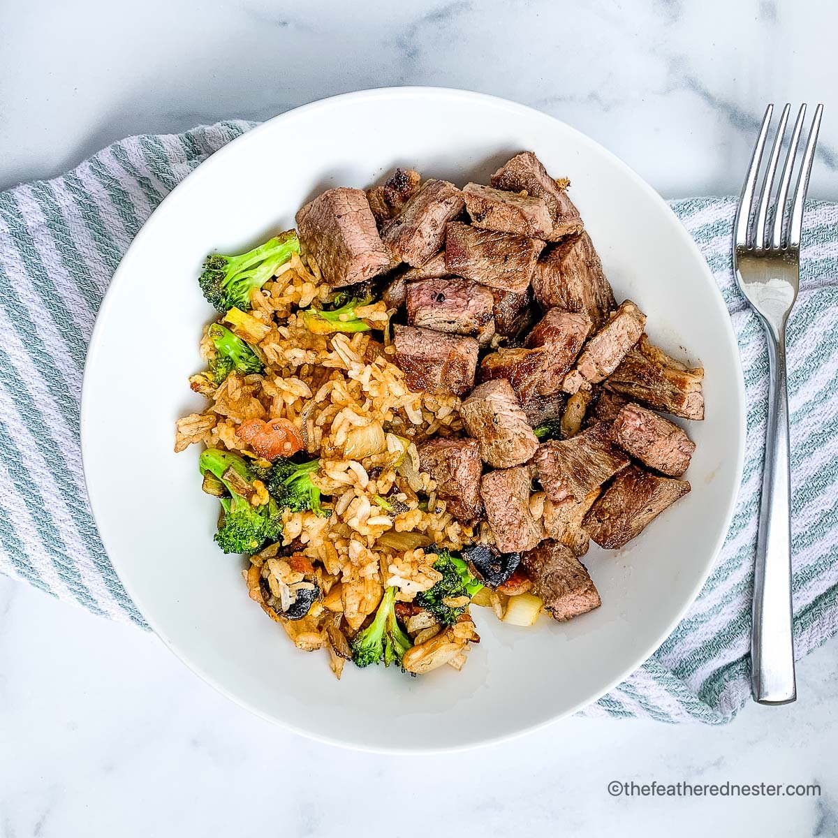 Dinner plate with pieces of steak and fried rice on the side.