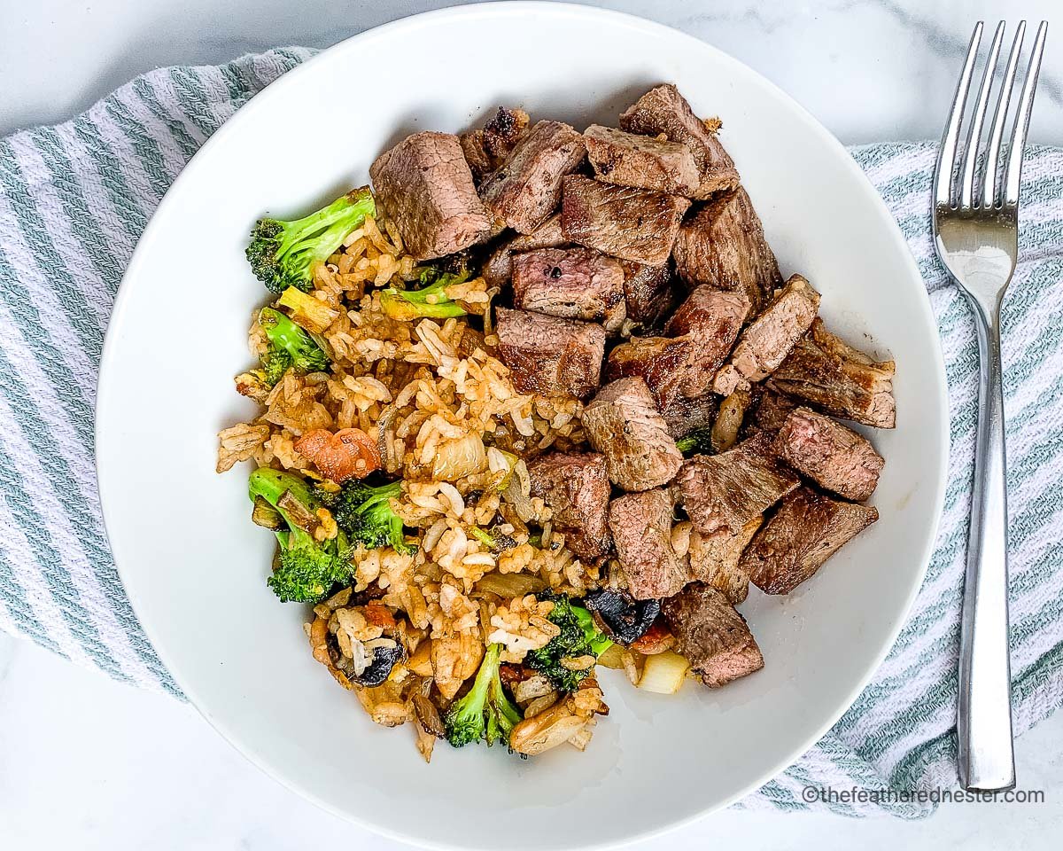 Chopped teppanyaki steak with fried rice on a white plate with silverware and a blue and white napkin.