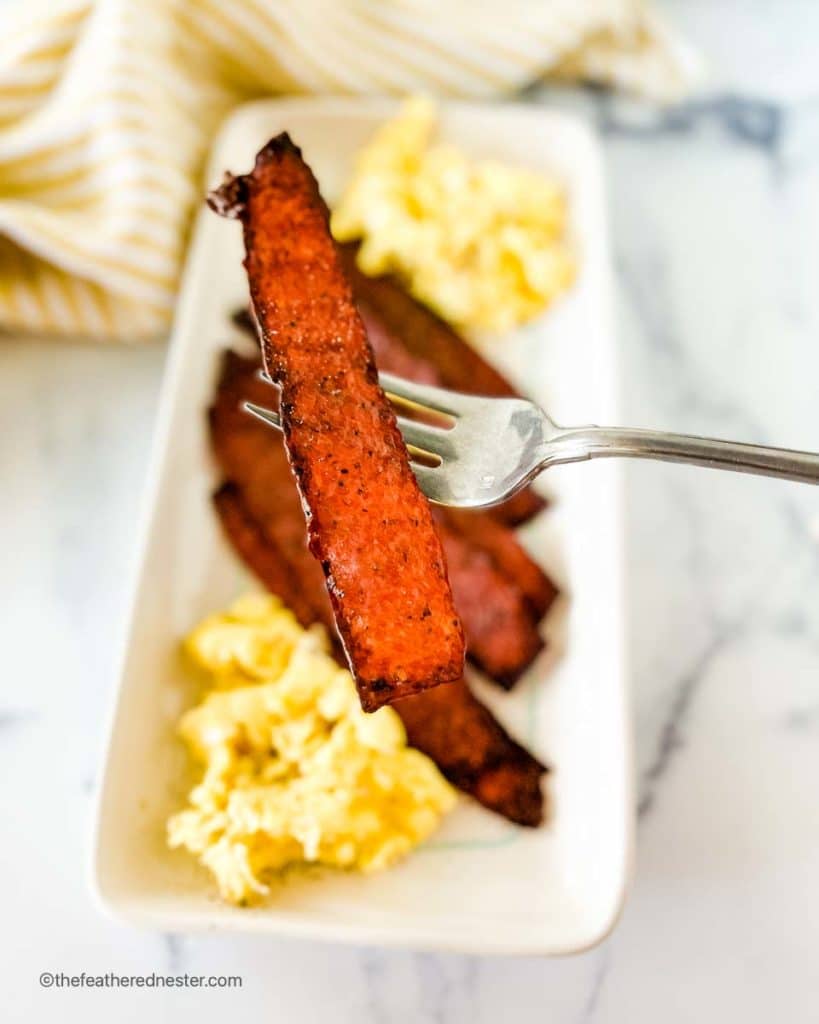 a white platter with oven baked turkey bacon and scrambled eggs
