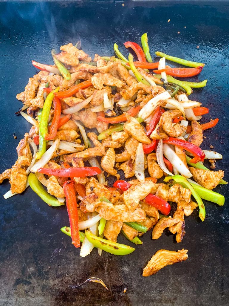 cooking combined marinated chicken fajitas and vegetables mix on a griddle