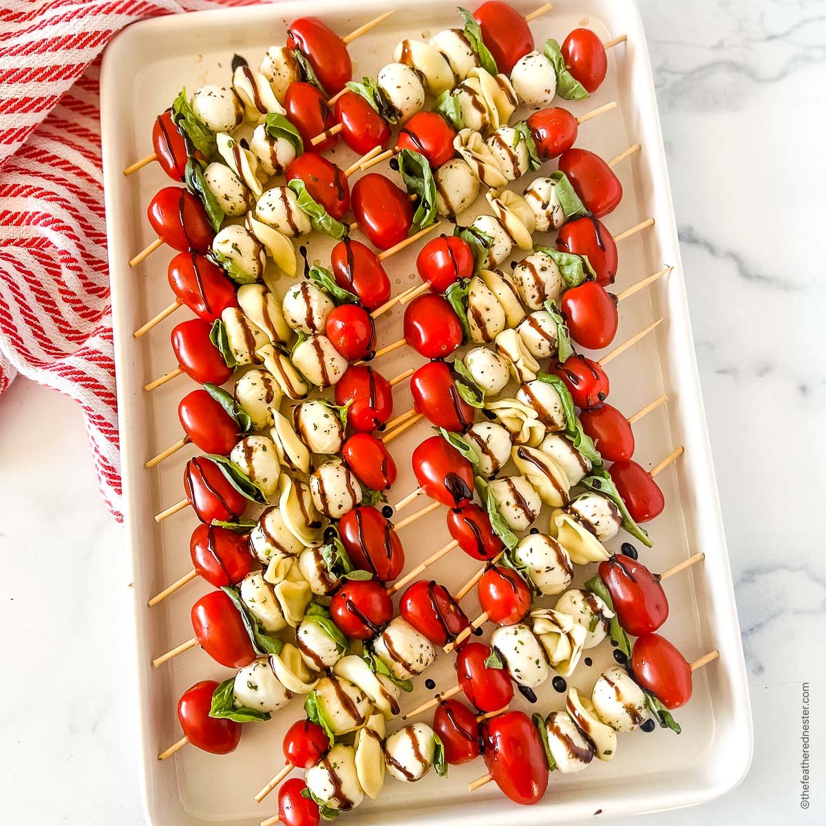 a white tray of kabob party appetizers with balsamic glaze on top of a red and white napkin.