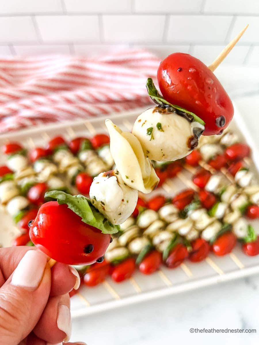 a closeup of a caprese kabobs with a tray of caprese skewers with balsamic glaze and a red and white napkin in the background.