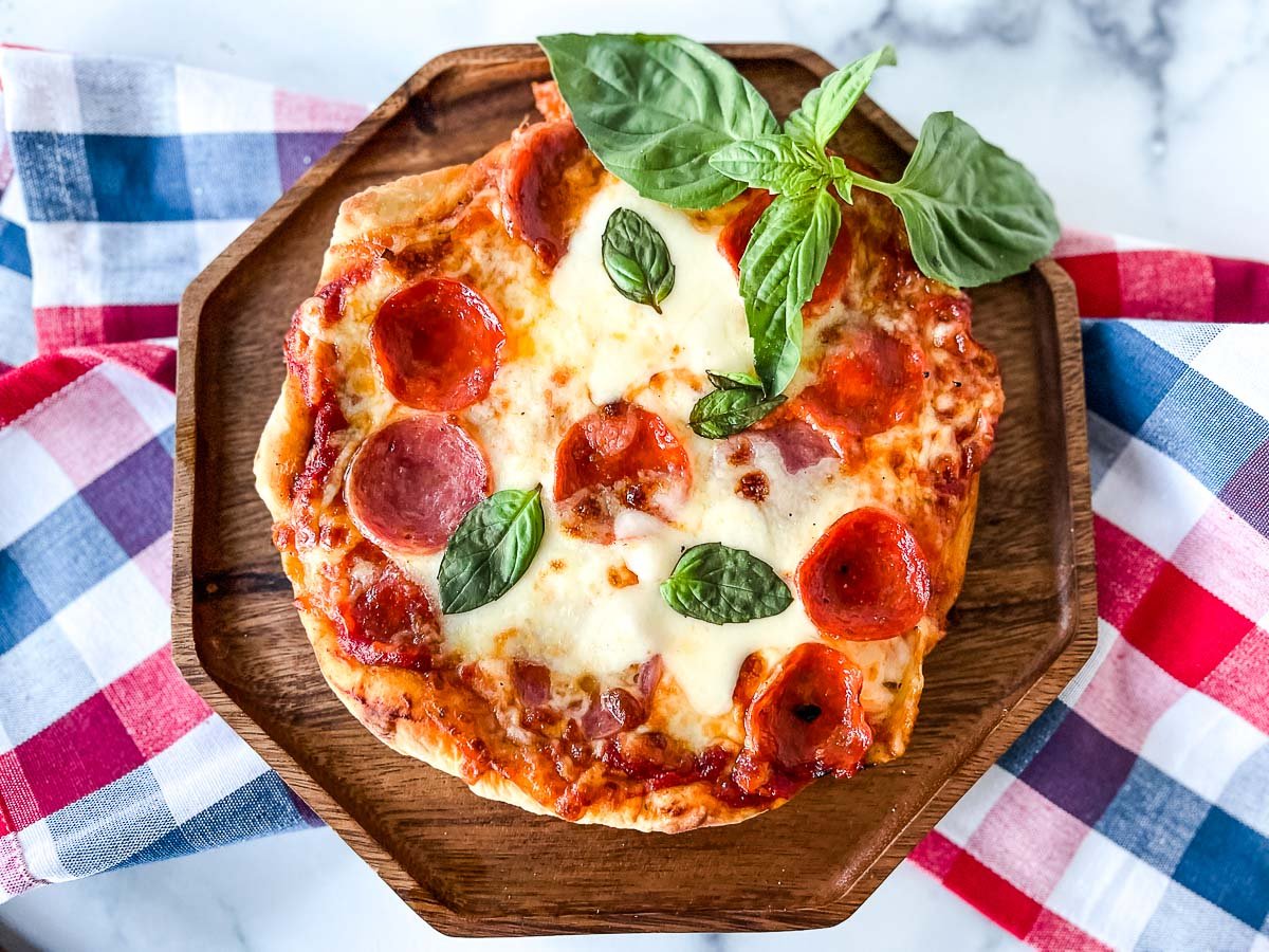 a fire grilled pizza on a wooden serving tray with a sprig of basil over a red, white, and blue napkin.