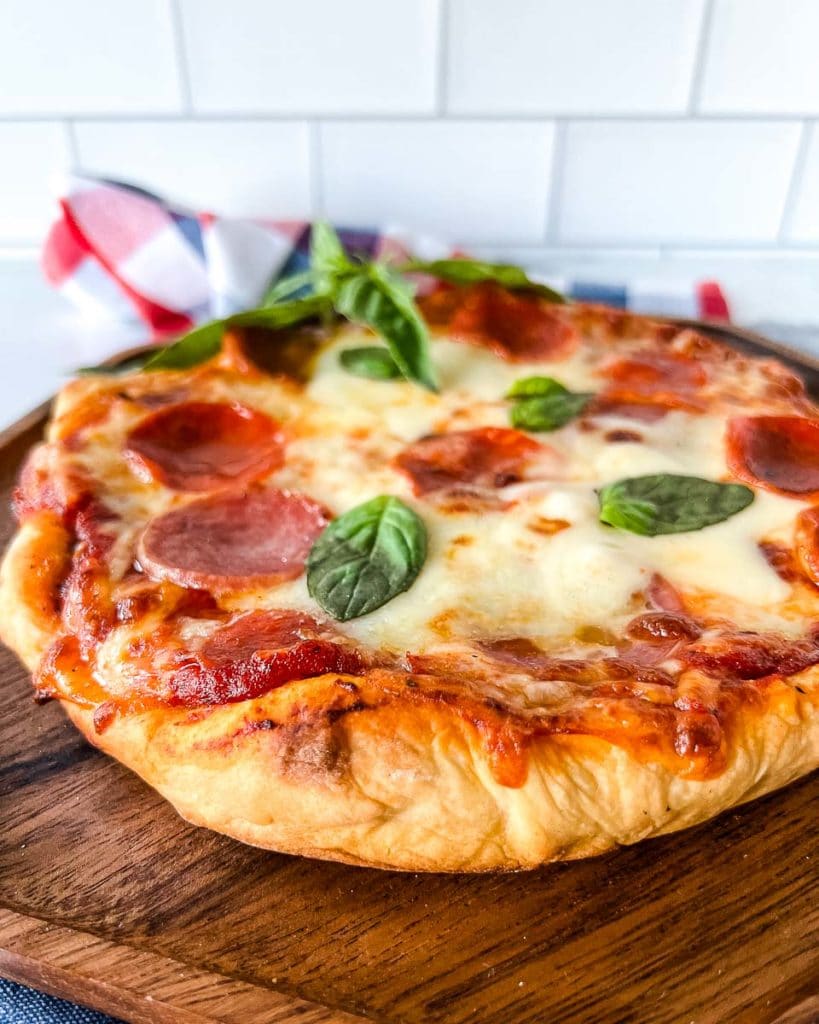 pizza on a wooden serving tray with a sprig of basil