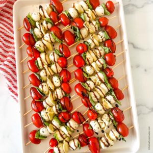 a white tray of kabob party appetizers with balsamic glaze on top of a red and white napkin