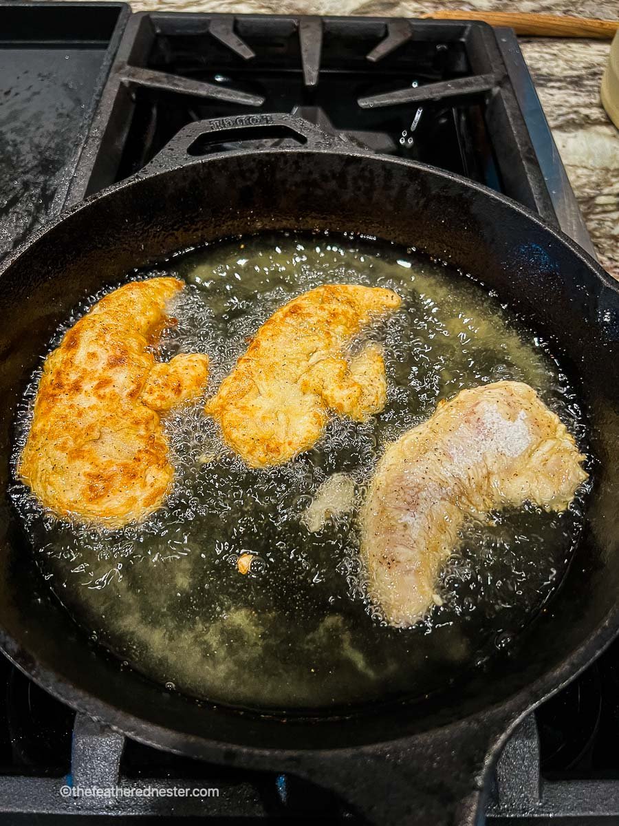 Frying the Nashville chicken tenders in the oil on a cast iron skillet.